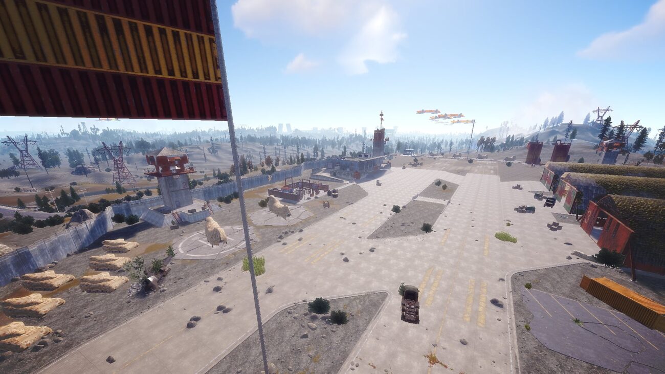 A wide paved compound with watchtowers, shipping containers, hay bales and power pylons, on the custom Rust map Apocalypse Spain
